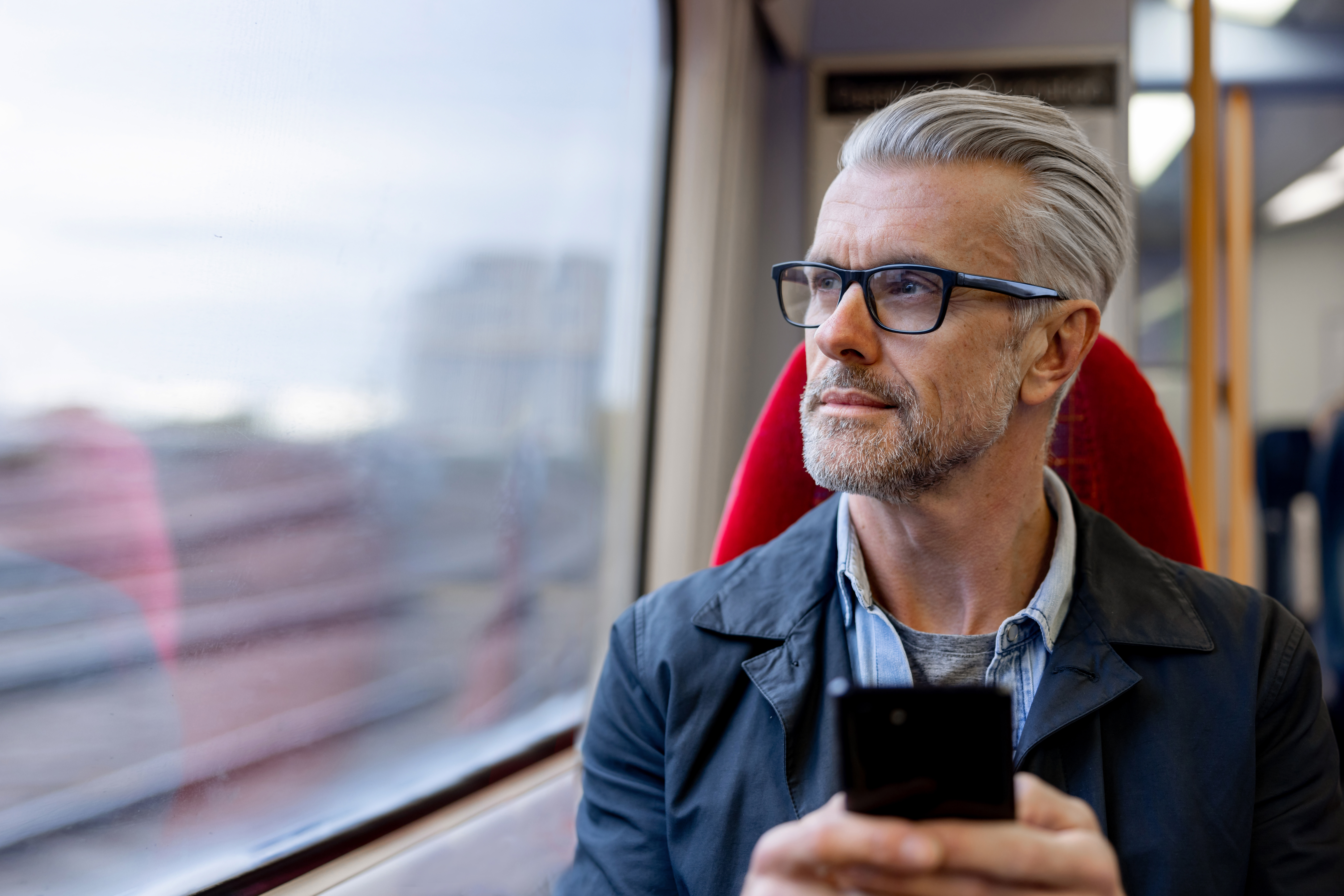 Man on a train holding a phone looking out the window