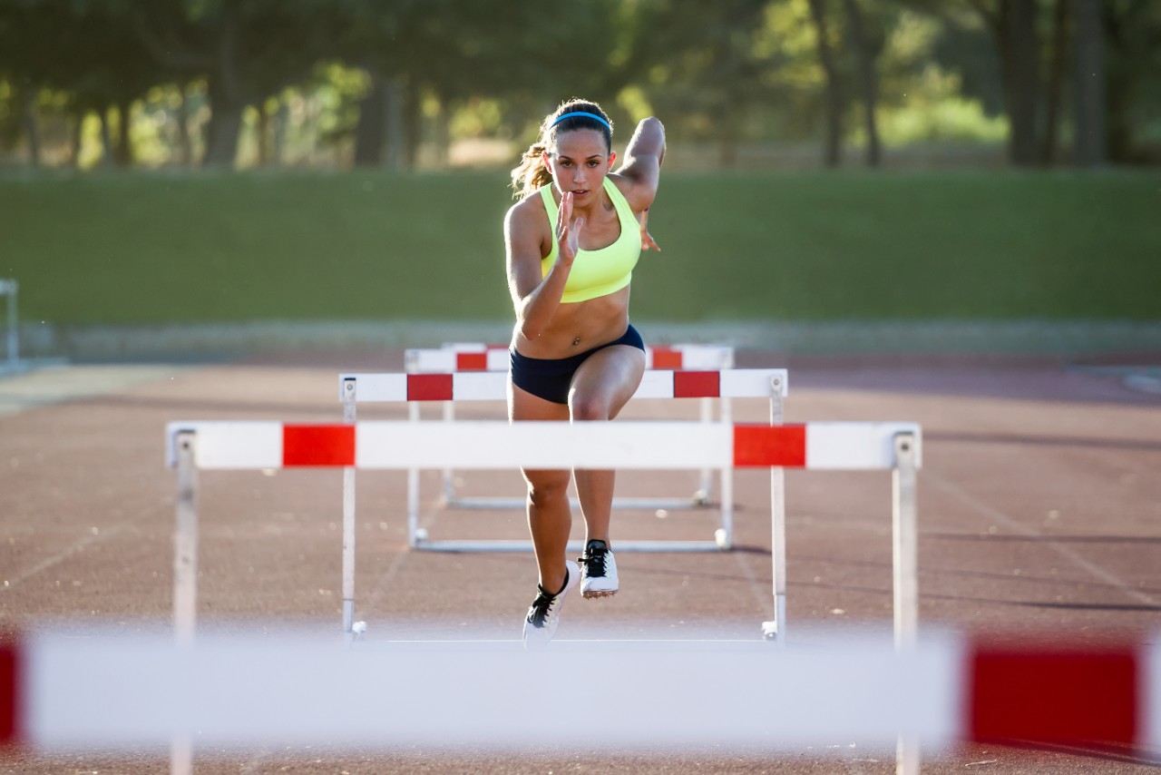 Portrait of young athlete jumping over a hurdle during training on race track.